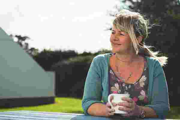 Mel from Highcliffe Holidays sits on a bench with a mug of tea.