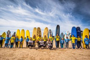 A large group of learner surfers pose with their boards on Polzeath beach, with instructors from Surfs Up Surf School.