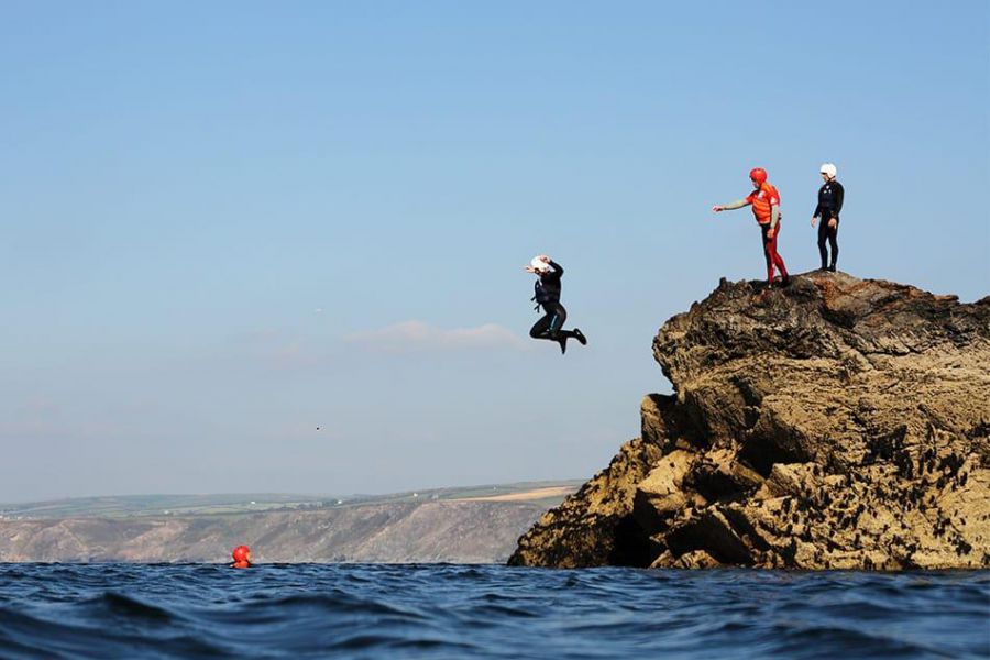 Holidaymakers jump into the sea from a rock after coasteering with Cornish Rock Tors, a company near Highcliffe.