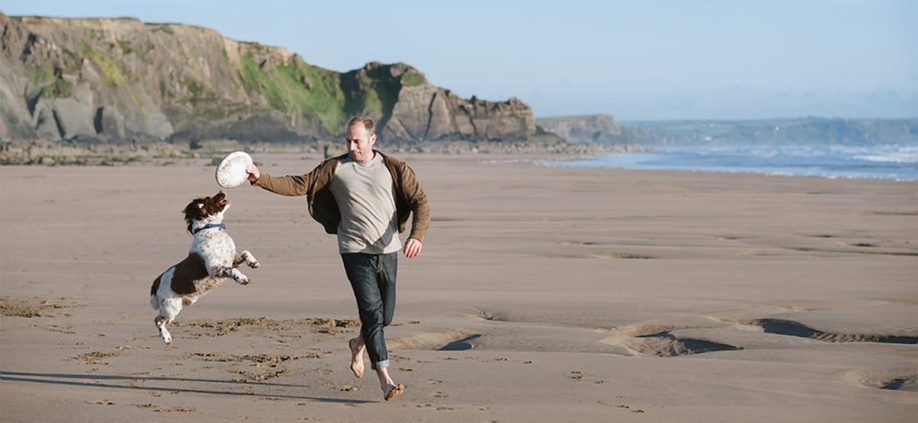 A man plays with his dog at Polzeath beach on the north Cornish coast whilst holidaying with Highcliffe Holidays.