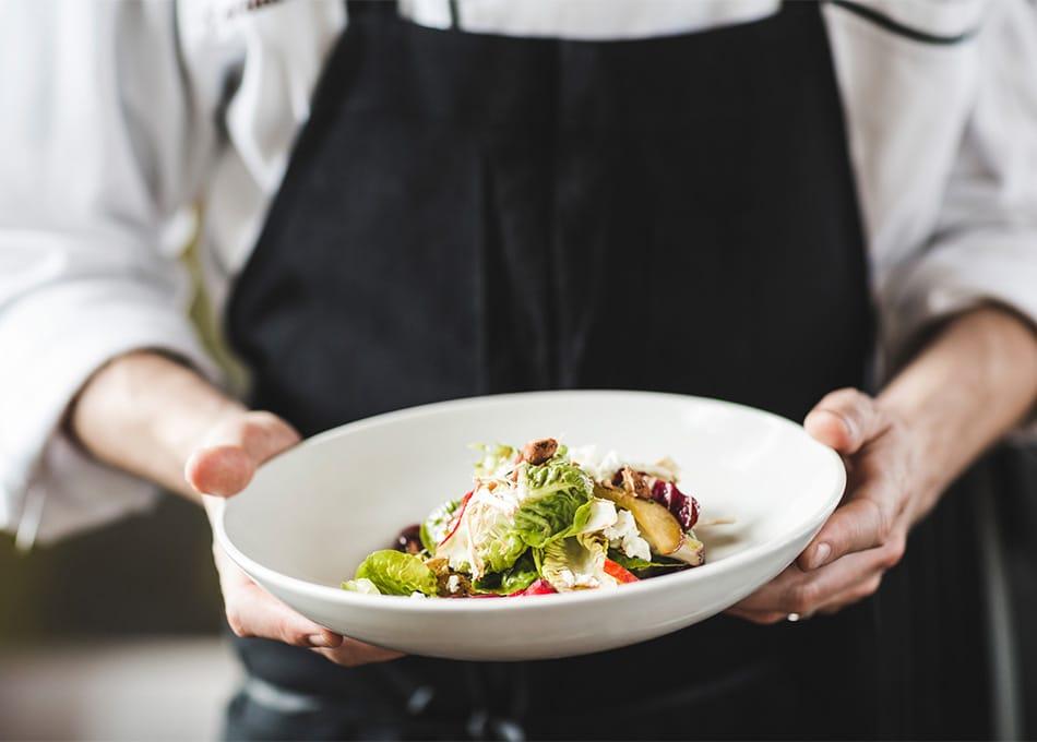 A chef holds a bowl of well-presented food.
